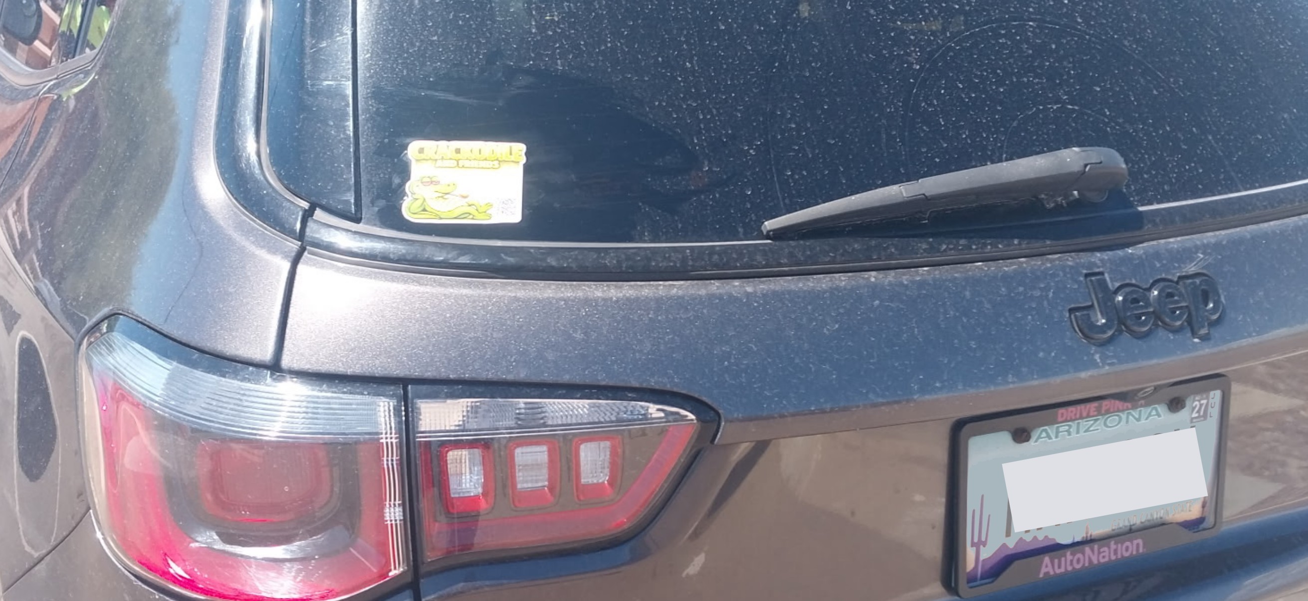 Crackodile and Friends sticker affixed to the rear window of a Jeep Grand Cherokee, Arizona parking lot, March 2026